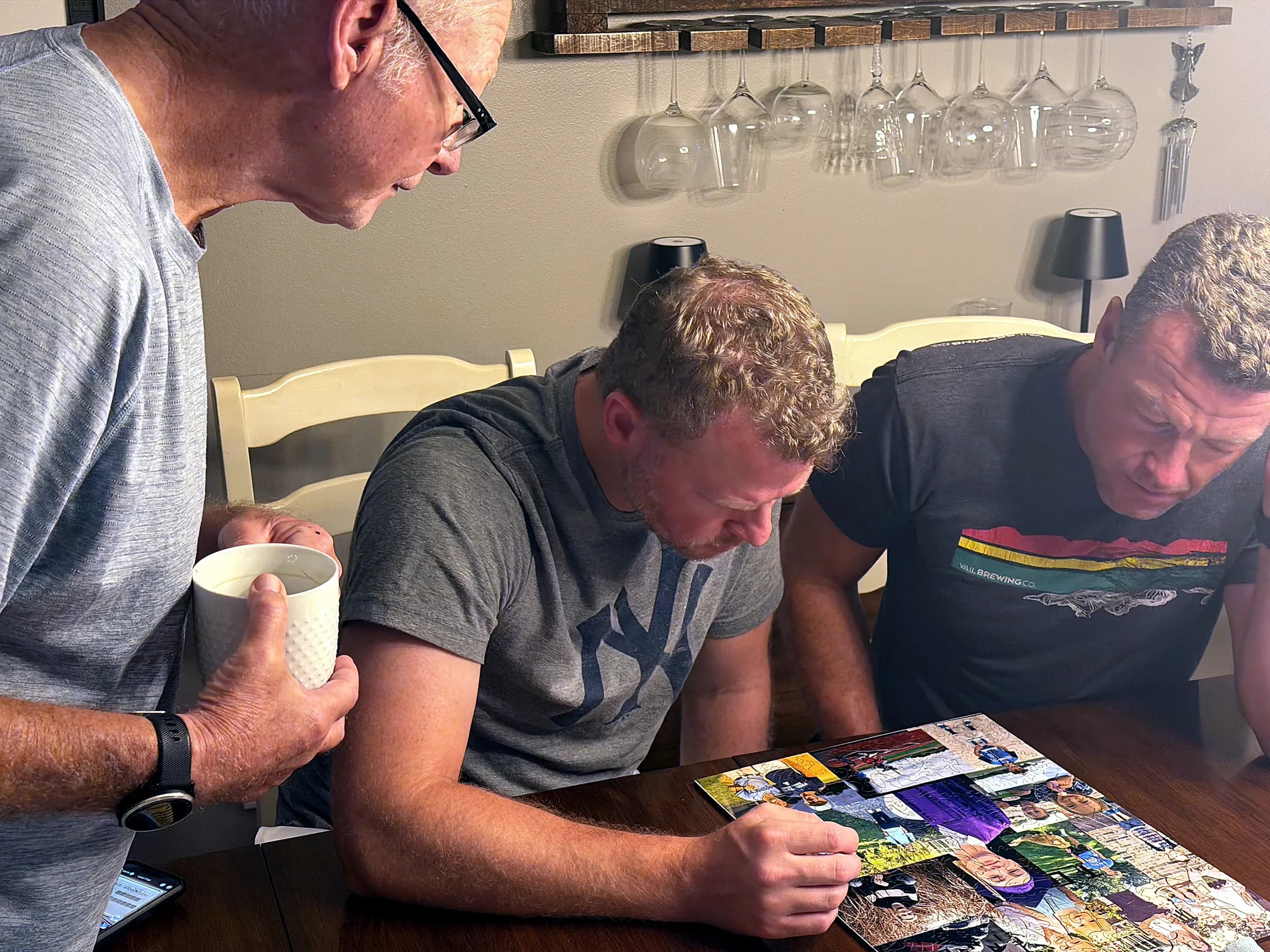 Three people leaning over a Whittled photo puzzle at a dining table, one placing a piece